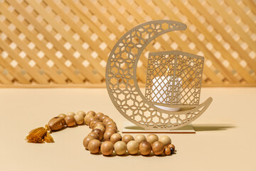 Decorative crescent with prayer beads and burning candle for Ramadan on beige table