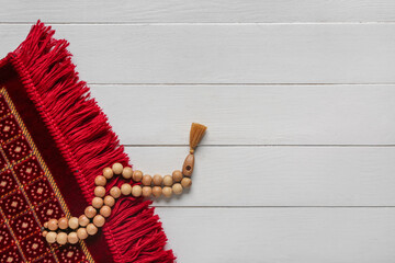 Prayer mat and beads for Ramadan on white wooden background