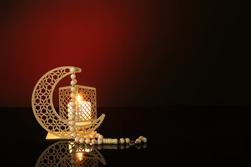 Decorative crescent with burning candle and prayer beads for Ramadan on dark red background