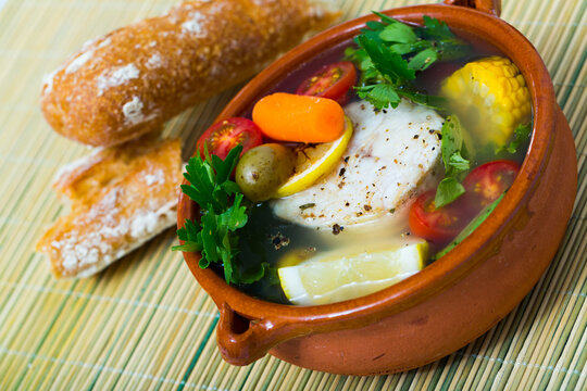Fisher soup from merluccius. Recipe: boil broth from fish head, add potatoes, carrots, shallots, corn, fish fillets or steak 200 g, season with salt, pepper. Then cook in oven at 200 deg for 40min