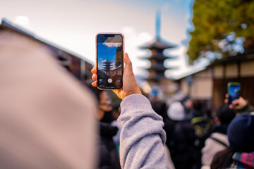 Yasaka Pagoda view and Hokan-ji Temple from Yasaka Dori street in Kyoto, Japan. Popular touristic street leading to Kyomizu Dera,Young female tourist taking photo with a mobile phone during sunset.