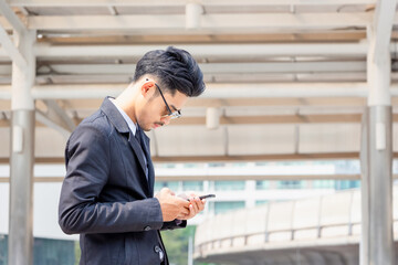 Young business man using mobile smartphone outside office with blurred city background