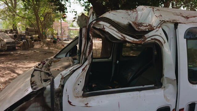 Wrecked white van with severe roof and body damage parked under a tree depicting a traffic accident aftermath accidental car