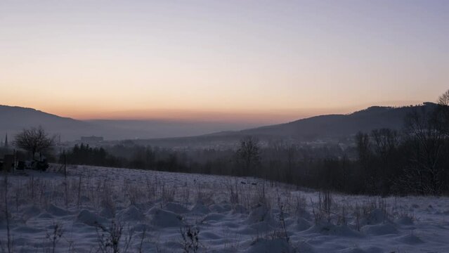 Night to day mist creeping across snowy Polish woodland with sun rising over mountain range, Bielsko-Biala, Poland