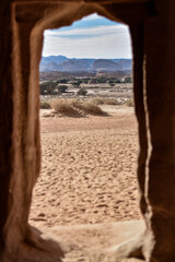 View of a landscape of mountains and desert from inside a house carved into the rock in the ancient city of Hegra.