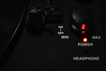 Detail shot of the power and volume knob on a record player with the power button illuminated. .
