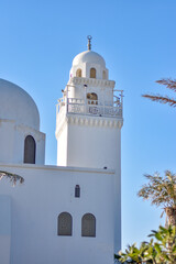 Minaret of a white mosque with blue sky in the background in the city of Jeddah.