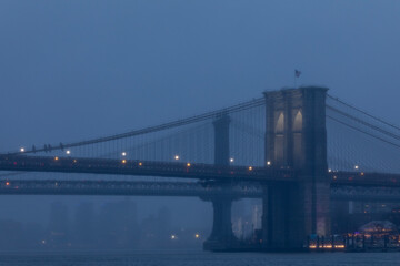 Fototapeta na wymiar Foggy evening view of the Brooklyn Bridge illuminated at dusk.