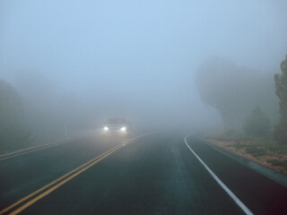 Lonely Car driving with headlights on a foggy road with low visibility 