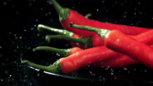 The chili peppers fall with splashes into the plate. On a black background. Filmed on a high-speed camera at 1000 fps. High quality FullHD footage