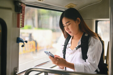 Young female commuter with backpack using mobile phone in public transportation