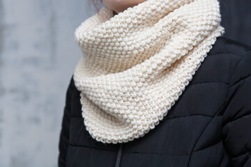 Cream colored handmade knitted textured snood scarf on a girl's neck close up