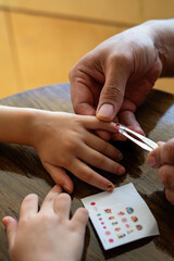 Father placing colourful nail stickers to the little girl's hand. Quality time at home.