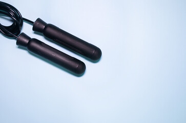 Black jump rope or skipping rope isolated on blue background. Sports, fitness, cardio, martial art and boxing accessories.