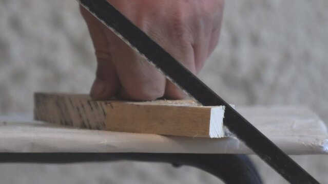 A man saws a wooden billet or part with a hacksaw on metal
