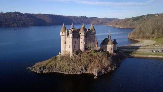 drone shot around chateau de val, french castle on the shore of the artificial lake of bort les les orgues on a sunny day during winter, Cantal departement, auvergne rhone alpes region, france