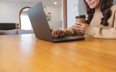 Closeup image of a young woman drinking coffee while working on laptop computer at home