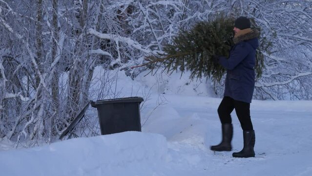 Man in a snowy environment throws the Christmas tree into the rubbish.