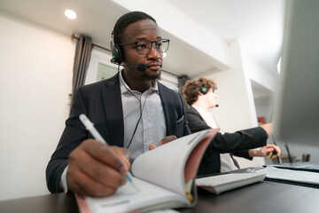 Close-up of motivated African American male teacher wearing headphones watching a webinar Writing...