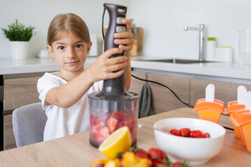 Portrait of cute child girl making ice cream. Kid have fun making with homemade fruit puree ice cream. Home made ice lollies. High quality photo