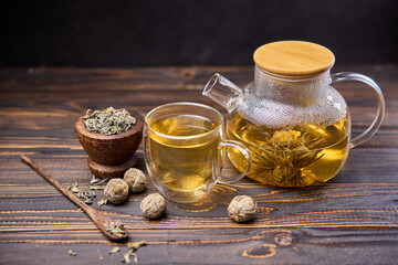 Teapot and glass cup with blooming tea flower inside on a wooden table