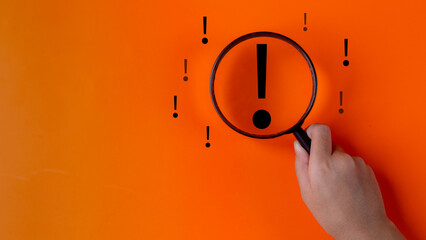 Magnifying glass focuses on an Exclamation mark icon over the orange background with copy space for...