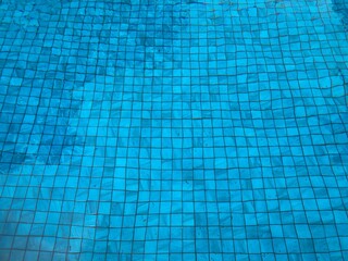 clear bright blue water in the outdoor swimming pool seeing small square tiles ground underneath it in full frame shot