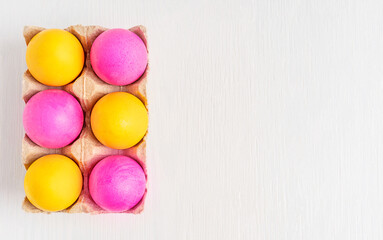 Top view of bright colourful easter eggs painted in pink and yellow colours in carton box on white wooden background with copy space boiled and prepared for holiday celebration as food and gift