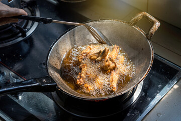 Cooking home cook style fast food menu. Marinated chicken wings fried crispy in a pan with boiling oil on gas stove in the kitchen.