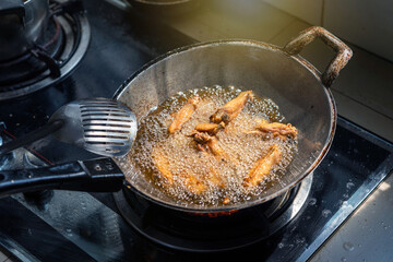 Cooking home cook style fast food menu. Marinated chicken wings fried crispy in a pan with boiling oil on gas stove in the kitchen.