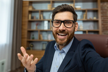 First person view of cheerful adult man in glasses having video call with happy facial expression...