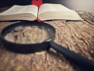 Opened bible with blurry magnifying glass and red heart in vintage background. Christian faith hope...