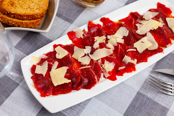 Delicious beef carpaccio with grated hard cheese served on plate. Meat appetizer..
