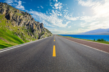 Asphalt highway road and green mountain with blue lake nature landscape at sunset