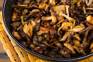 Fototapeta premium Appetizing mushrooms freshly fried in oil with onion and vegetables on frying pan