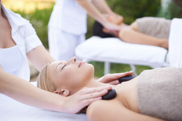 Women, hands and massage with hot stone in spa, outdoor and wellness on bed for body treatment....