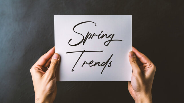 Holding white paper sheet with text Spring Trends, on black background