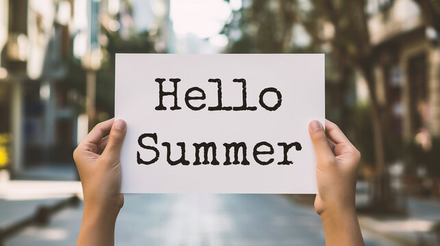 Closeup of hands holding paper with Hello Summer text on blurred background