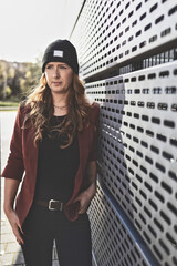 Woman in her mid-thirties with long red hair wearing black clothing with a brown jacket and hat in an urban environment.