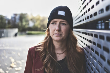 Woman in her mid-thirties with long red hair wearing black clothing with a brown jacket and hat in...