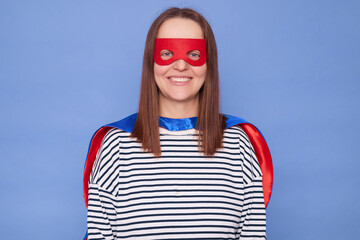 Smiling Caucasian brown haired woman wearing superhero costume and striped shirt isolated over blue...