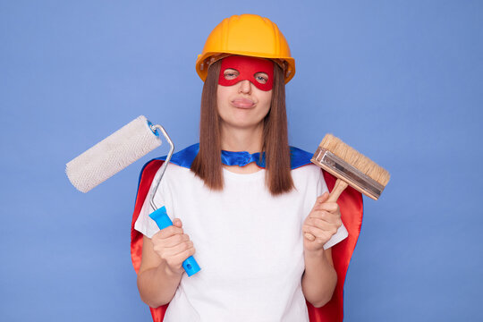 Painting profession. Renovation worker. Craftsman painter skills. Sad tired disappointed woman painter wearing superhero costume and protective helmet holding painting roller and brush