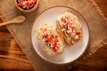 Molletes. Mexican recipe based on bolillo bread split lengthwise, spread with refried beans and gratin cheese, adding pico de gallo sauce and some protein such as ham, bacon or chorizo.