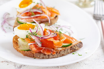 Delicious toast with salmon, boiled egg, cucumber and cream cheese on a white plate. Healthy eating, breakfast. Keto diet food. Tasty food.