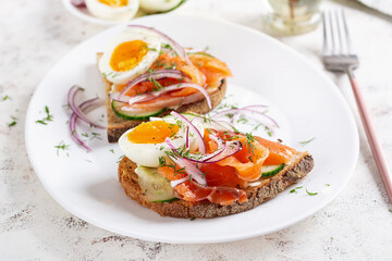 Delicious toast with salmon, boiled egg, cucumber and cream cheese on a white plate. Healthy eating, breakfast. Keto diet food. Tasty food.