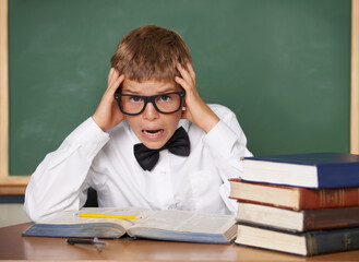 Boy child, stress and portrait with books, classroom and anxiety for exam, assessment and studying for knowledge. Student kid, notebook and learning for education, development and glasses at table