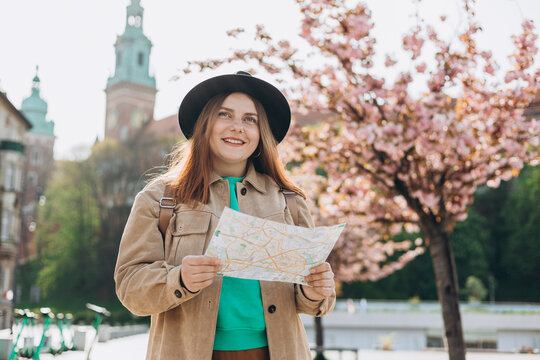 Attractive young female tourist is exploring new city. Redhead 30s girl holding a paper map in Krakow. Traveling Europe in spring. High quality photo