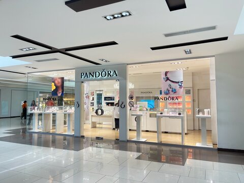 Pandora branded jewelry store in shopping mall. Glass pavilion, sign with logo on entrance, advertising image with new collection on showcase. Shop of famous chain featuring with variety of bijouterie