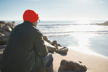 Rear view of young man, depression and stress looking at the sea on a beach at sunrise. Tired...