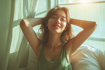 An attractive Asian woman wearing green casual clothes stretches after waking up in bed. Lazy girl activities on Sunday morning